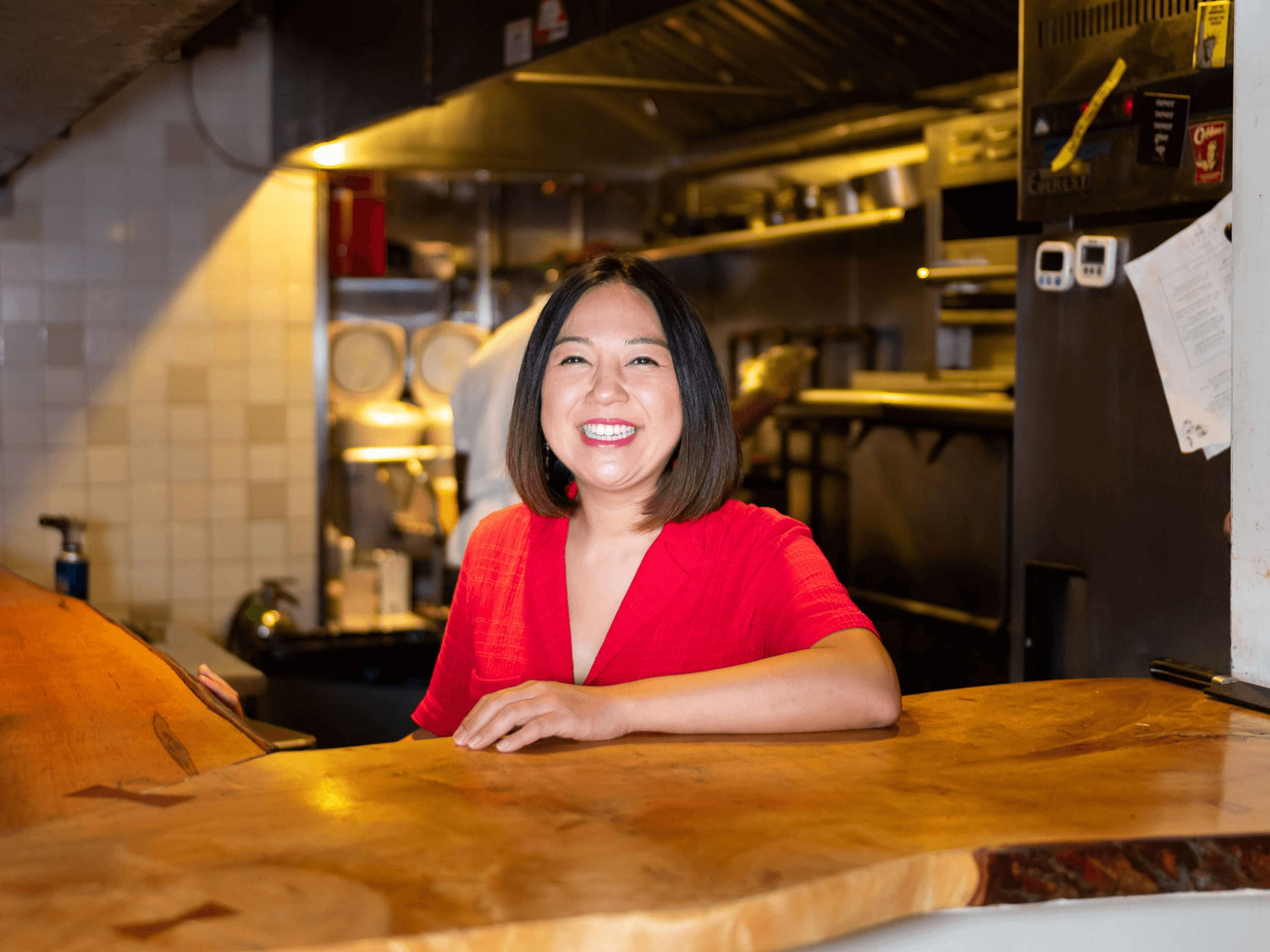 A smiling woman stands in a restaurant kitchen.